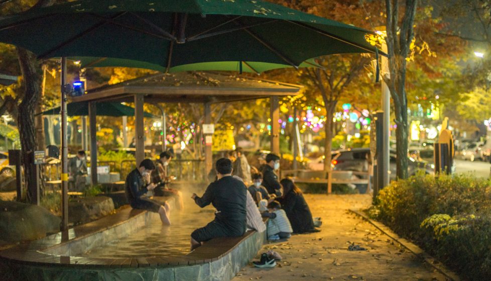 People sitting with their feet in a hot spring inside a park at night
