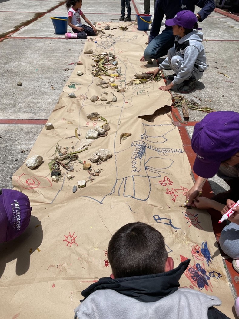 Un grupo de niños dibujando en un gran papel marrón extendido afuera sobre el concreto.