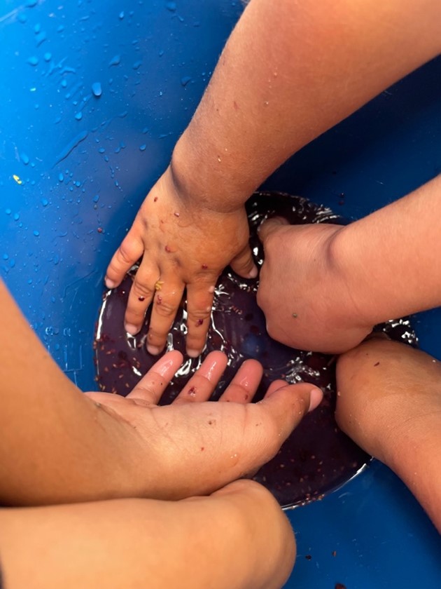 Multiple hands reaching into a blue bucket with dark water inside