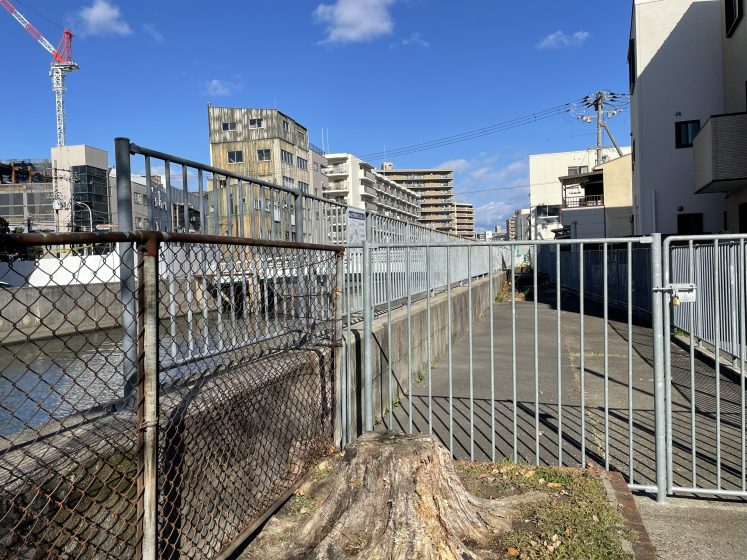 A metal gate blocking off a paved path next to a manmade waterway
